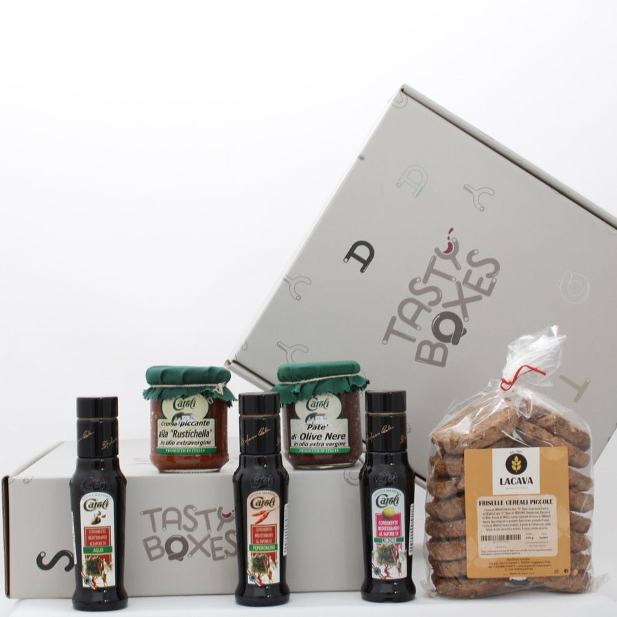 L'immagine mostra la Box Gusto Mediterraneo di TastyBoxes, che contiene un vasetto di crema piccante alla "Rustichella", un vasetto di patè di olive nere e 3 bottigliette da 100ml di olio aromatizzato ai gusti aglio, peperoncino e limone dell'azienda agricola Caroli, e una confezione di friselline pugliesi ai cereali del Panificio Lacava 